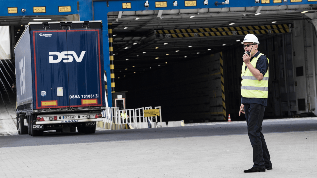 Operatør snakker i walkie talkie, mens DSV-lastebil kjører ombord ferje i bakgrunnen.